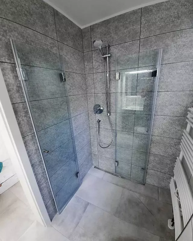 Eckdusche mit Falttüren F1W aus Glas in Badezimmer mit grauer Rückwand und Boden