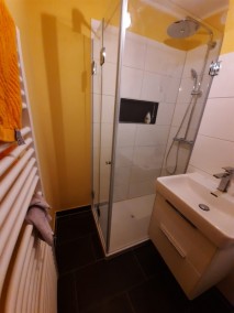 Dusche mit Falttüren F1S aus Glas in Bad mit schwarzen Bodenfliesen und gelber Wand