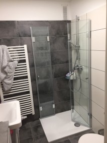 Dusche mit Falttüren F1W aus Glas auf Flach Duschwanne vor grau und weiß gefliester Wand